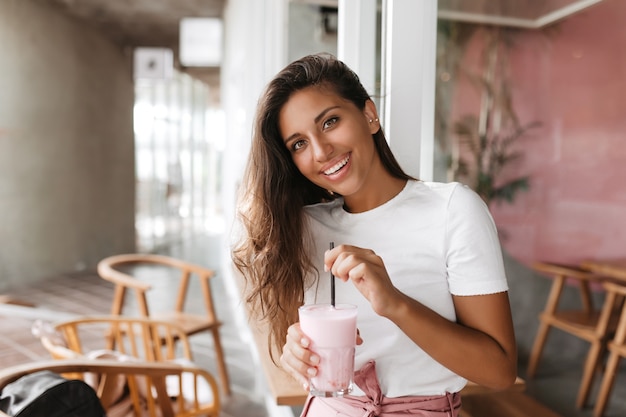 La mujer está sentada en un acogedor café y revuelve su batido de fresa