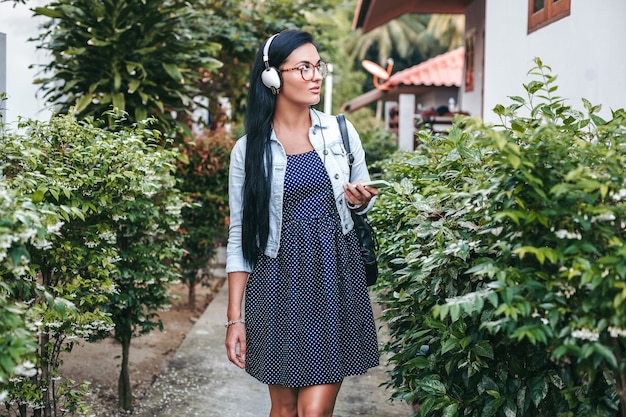 Mujer con estilo joven caminando con smartphone, escuchando música en auriculares, vacaciones de verano