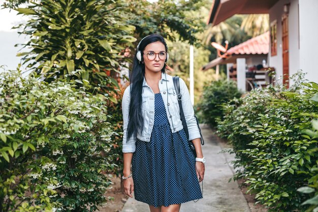 Mujer con estilo joven caminando con smartphone, escuchando música en auriculares, vacaciones de verano