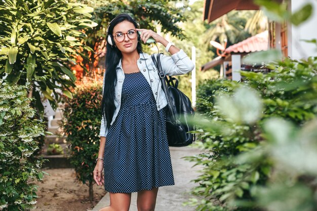 Mujer con estilo joven caminando con smartphone, escuchando música en auriculares, vacaciones de verano