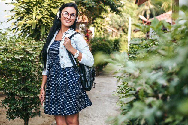Mujer con estilo joven caminando con smartphone, escuchando música en auriculares, vacaciones de verano