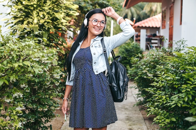 Mujer con estilo joven caminando con smartphone, escuchando música en auriculares, vacaciones de verano