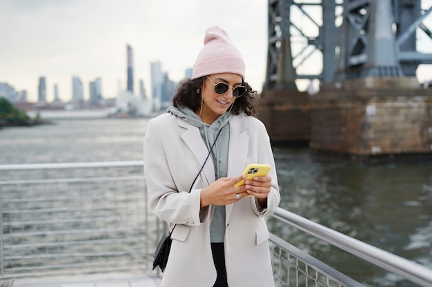 Mujer con estilo joven con smartphone al aire libre mientras explora la ciudad