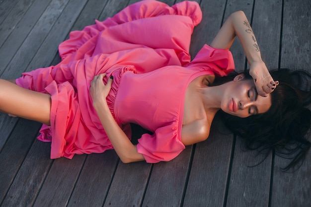 Mujer de estilo de verano al aire libre, retrato de moda soleado de mujer sensual con vestido rosa en la puesta de sol de la playa en la orilla del mar