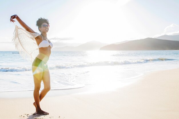 Mujer estirando los brazos en la playa con rayos de sol