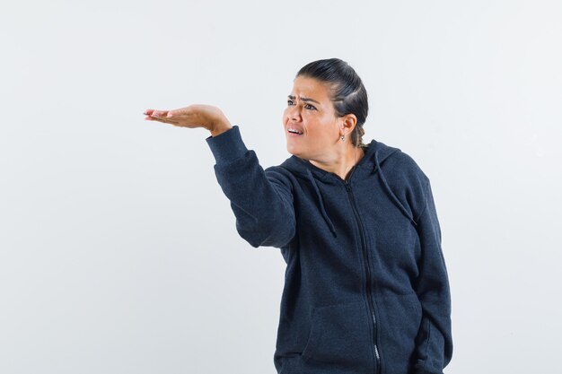 Mujer estirando la mano en forma de interrogación en sudadera con capucha y con enojo. vista frontal.