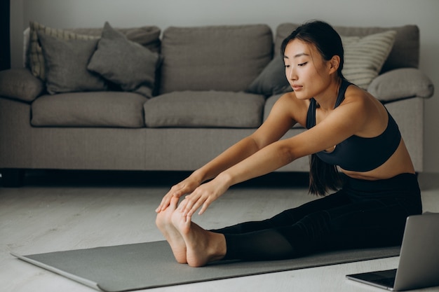 Mujer estirando sobre estera de yoga en casa