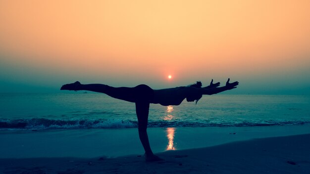 Mujer estirando su cuerpo en poses de yoga al atardecer en la playa