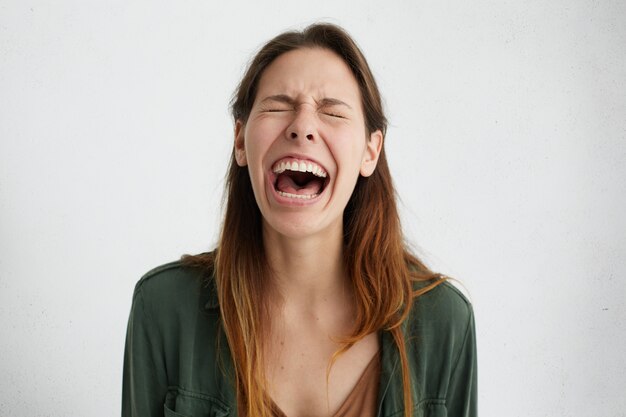 Mujer estresante cerrando los ojos mientras llora después de haber abierto la boca sintiendo tensión mirando molesto por el dolor.