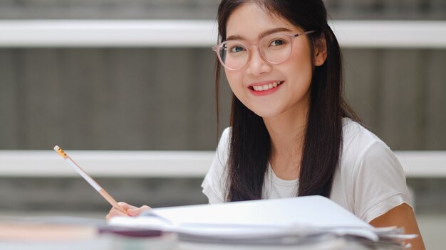 Mujer estudiante asiática leyendo libros en la biblioteca de la Universidad