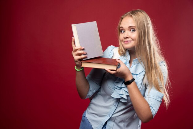 Mujer estudiante rubia sostiene sus libros y se siente feliz.