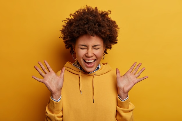 Foto gratuita mujer étnica rizada llena de alegría levanta las palmas, se ríe positivamente