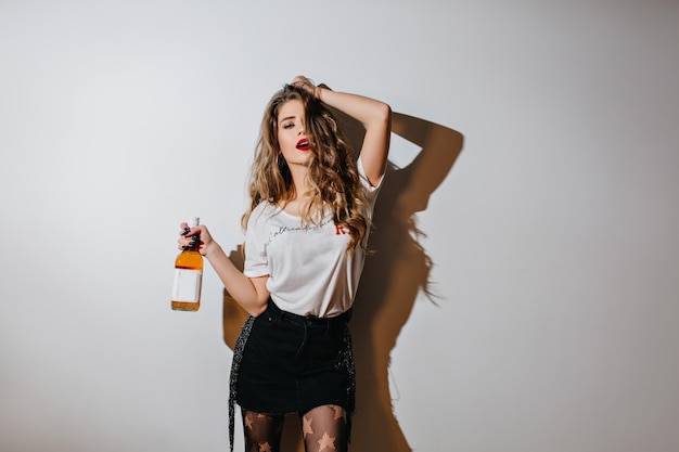 Foto gratuita mujer europea cansada mirando a la cámara, sosteniendo una botella de bebida alcohólica