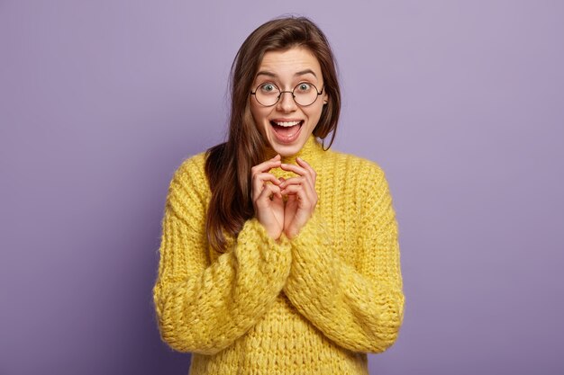 La mujer europea feliz alegre mantiene las manos juntas, sonríe positivamente