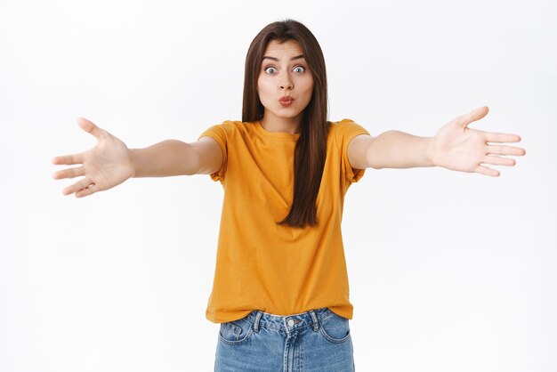 Una mujer europea guapa y tonta con una camiseta amarilla extendió las manos hacia los lados y besó los labios mientras esperaba que alguien cayera en sus brazos para acurrucarse coqueta sobre fondo blanco