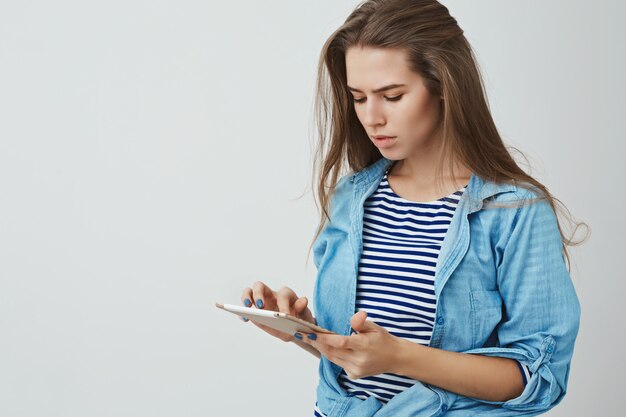 Mujer europea moderna joven elegante de moda seria que sostiene la tableta digital