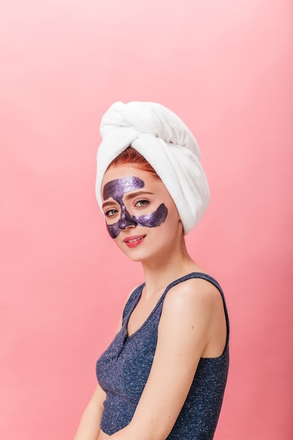 Mujer europea refinada posando con mascarilla. Disparo de estudio de niña caucásica con toalla en la cabeza.