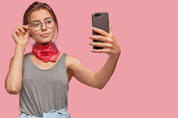 Mujer europea satisfecha toma imágenes en un teléfono celular moderno, comparte en blog