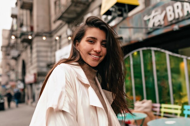 Mujer europea con sonrisa feliz y cabello oscuro sonriendo a la cámara y caminando con emociones felices