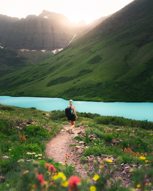 Foto gratuita mujer excursionista con una mochila caminando por un camino estrecho en un hermoso campo verde junto a un río