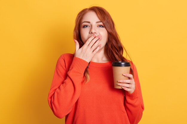 Mujer exhausta y somnolienta tiene noche de insomnio de preparación para el examen, bosteza y se tapa la boca con café para llevar bebidas de palma para sentirse refrescada