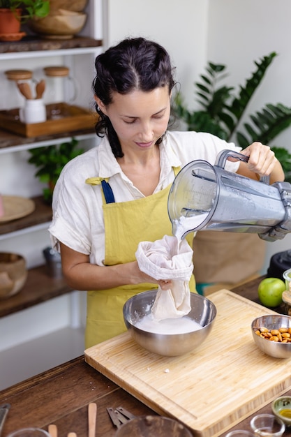 Mujer exprimiendo la leche de almendras de almendras en la cocina de casa