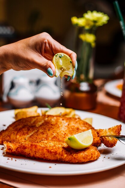 Mujer exprimiendo limón sobre pescado crujiente de papas fritas