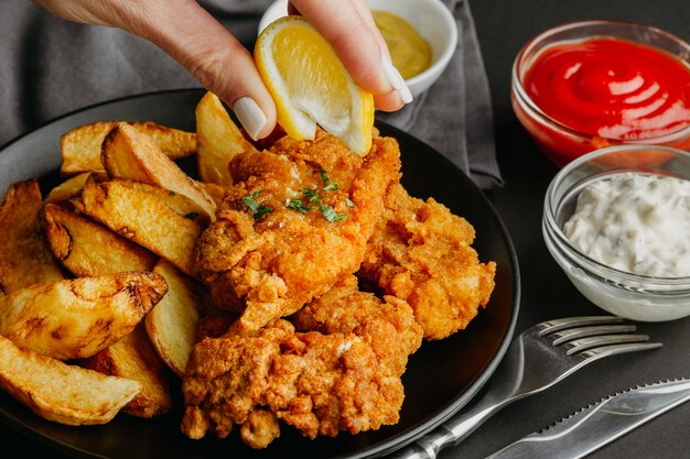 Mujer exprimir jugo de limón en un plato de pescado y patatas fritas