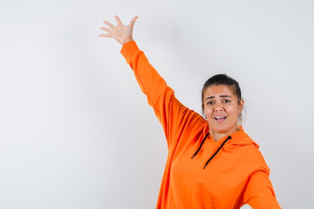 Mujer extendiendo los brazos a un lado en sudadera con capucha naranja y mirando feliz