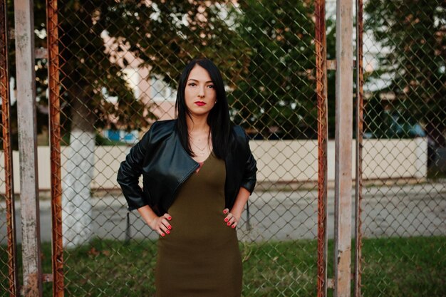 Mujer fabulosa en vestido y chaqueta de cuero de pie junto a la red