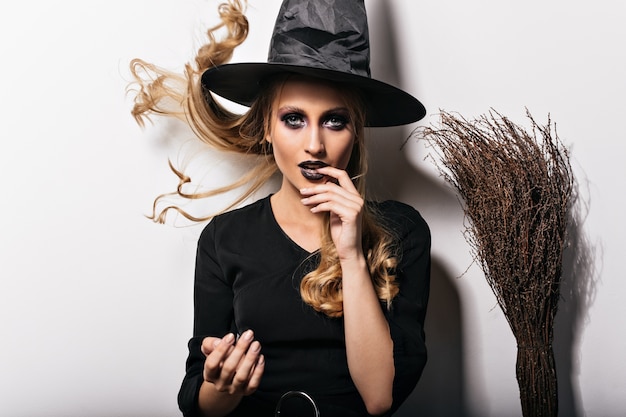 Mujer fascinante con maquillaje negro disfrutando de carnaval. foto de la chica rubia de moda en traje de halloween.