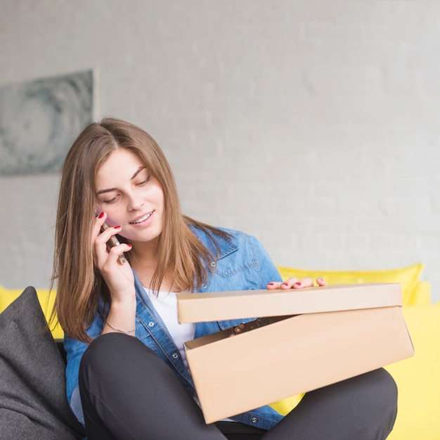 Mujer feliz abriendo su regalo de cumpleaños mientras hablaba por teléfono inteligente