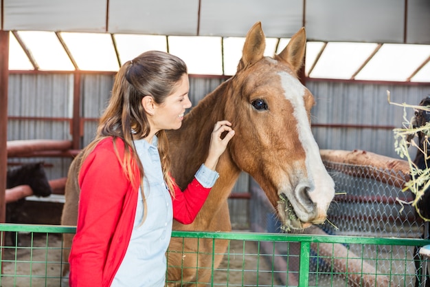 Foto gratuita mujer feliz acariciando al caballo en el establo