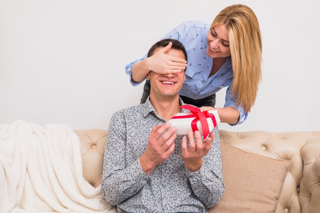 Mujer feliz con los actuales ojos cerrados al hombre sonriente en el sofá