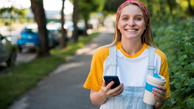 Mujer feliz al aire libre con teléfono inteligente y taza