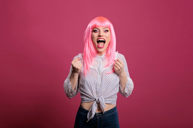 Mujer feliz y alegre que se siente emocionada por ganar, gritar y celebrar la victoria con los brazos levantados. Animando con entusiasmo por el éxito y el triunfo, disfrutando de la suerte en el estudio.