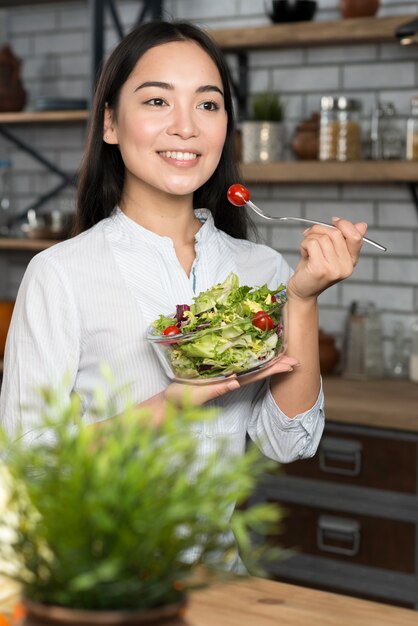 Mujer feliz asiática joven que come la ensalada verde sana