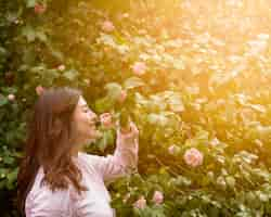 Foto gratuita mujer feliz atractiva que sostiene el crecimiento rosado de la flor en la ramita verde