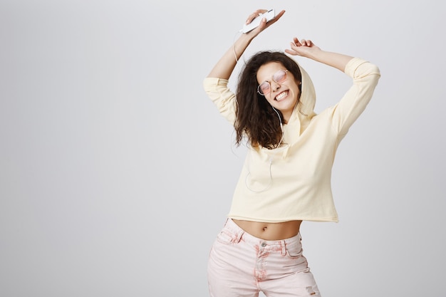 Mujer feliz bailando y disfrutando de la música en auriculares, sosteniendo smartphone