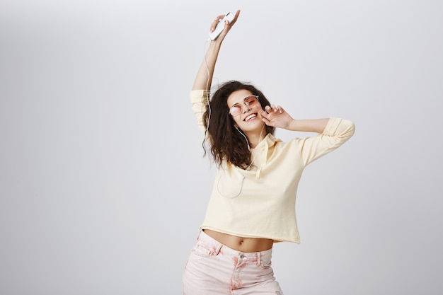 Mujer feliz bailando y disfrutando de la música en auriculares, sosteniendo smartphone