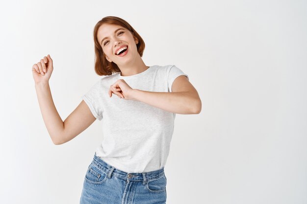 Mujer feliz bailando y divirtiéndose, riendo alegre, de pie contra la pared blanca