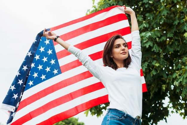 Mujer feliz con bandera americana en la naturaleza