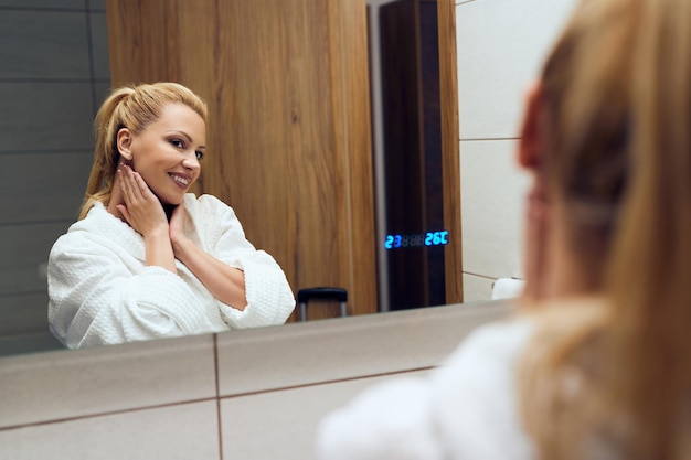 Mujer feliz en una bata de baño mirándose en un espejo en el baño