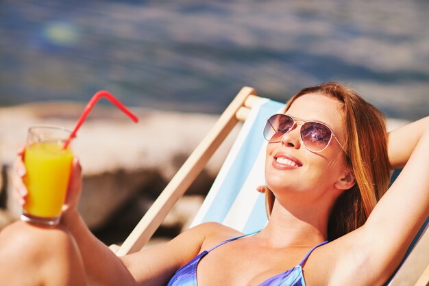 Mujer feliz bebiendo un zumo de naranja en la playa