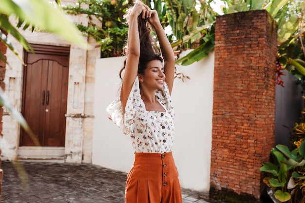 Mujer feliz en blusa blanca y falda naranja levanta las manos