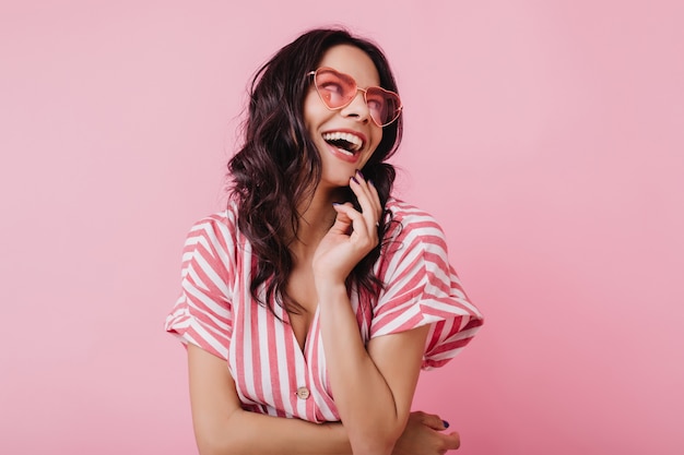 Mujer feliz con cabello castaño ondulado riendo. Chica jocund en traje rosa a rayas sonriendo.