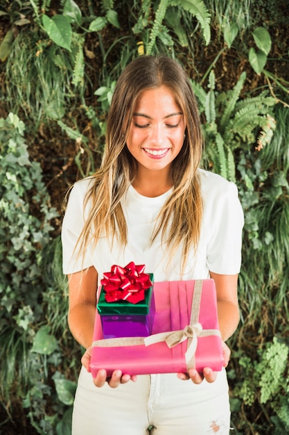 Mujer feliz con cajas de regalo de pie contra el fondo de hojas verdes