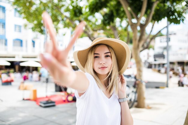 Mujer feliz en la calle soleada que muestra el signo de la paz.