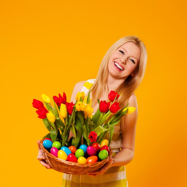 Mujer feliz con canasta con flores de primavera y huevos de pascua