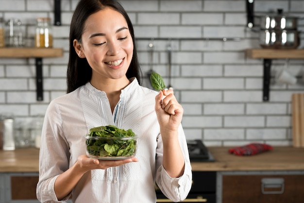 Mujer feliz con la celebración de hojas de albahaca verde en la cocina